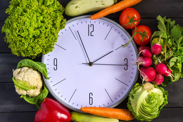 Clock and fresh vegetables. Zucchini, bell peppers, carrots, cabbage, cauliflower, radish, lettuce, tomato. Concept of a healthy diet. Copy space.