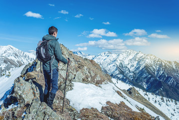 Hiker with trekking poles stands in the snowy mountains at the foot of the peak. Concept of travel and achieve the goal