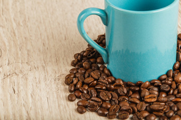 Grains of coffee on a wooden background in large quantities and a cup