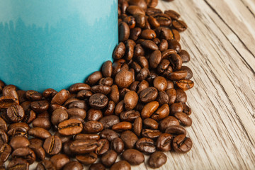 Grains of coffee on a wooden background in large quantities and a cup