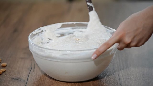 Chef with spatula stirring macaron batter or cream in bowl at pastry shop.