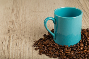 Grains of coffee on a wooden background in large quantities and a cup