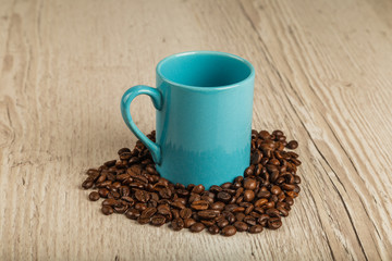 Fototapeta na wymiar Grains of coffee on a wooden background in large quantities and a cup