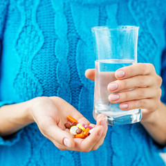 The person holds the medicine and a glass of water in his hands. Square. Concept illness, colds, cure, fall and winter.
