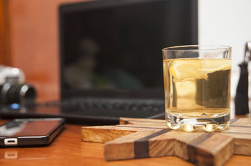 Delicious tea with lemon in a transparent glass on the table next to the phone and laptop