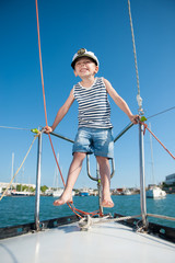 smiling funny little boy in a captain's hat playing on board yacht