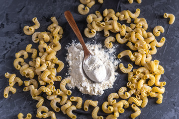 Uncooked pasta cavatappi with flour from durum wheat on a dark background. Concept of The composition of food design.