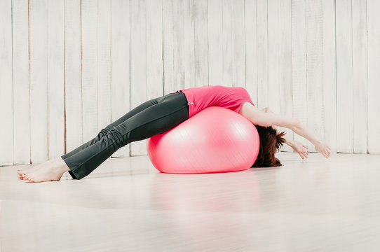 a girl holding balance lying pose over a pink fitball in a gym