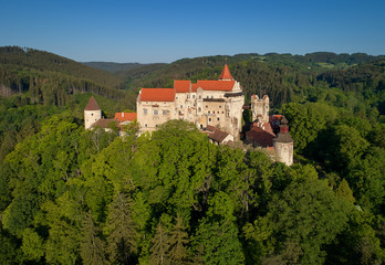 Fototapeta na wymiar Moravian castle Pernstejn, standing on a hill above deep forests of the Bohemian-Moravian Highlands against blue sky. Aerial photography. Ancient royal castle in Czech landscape, czech travel place.