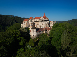 Moravian castle Pernstejn, standing on a hill above deep forests of the Bohemian-Moravian Highlands against blue sky. Aerial photography. Ancient royal castle in Czech landscape, czech travel place.