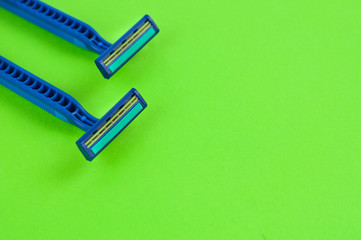 Two new blue plastic disposable razors with two blades and humid strip on blank green paper