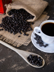 cup and bag with coffee beans coming out of the bag on the stone table and wooden spoon