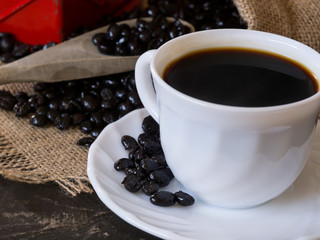 cup with coffee beans coming out of the bag on the stone table and wooden spoon