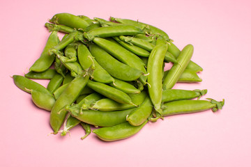 Fresh green ripe sugar snaps, sweet peas copy space close up on light pink background