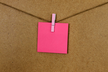 Hoja de papel de color rosa (posit), sujeto con una pequeña pinza de colore rosa con puntitos...
