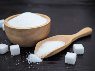 Wooden bowl and spoon with sugar cube on dark wood background.
