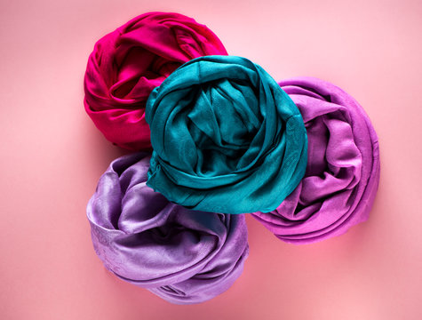 Various silk and woolen scarves on a pink background, top view