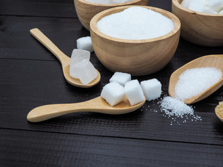Wooden bowl and spoon with sugar cube on dark wood background.