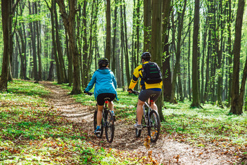Naklejka premium couple riding bicycle in forest in warm day. view from behind
