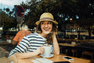 Young woman with a cup of coffee sitting in a cafe, photographed from the street, freelance concept