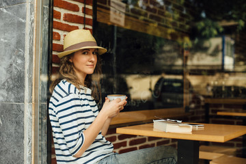 Young woman with a cup of coffee sitting in a cafe, photographed from the street, freelance concept
