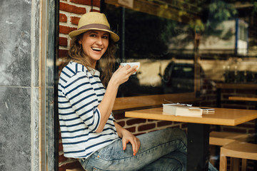 Young woman with a cup of coffee sitting in a cafe, photographed from the street, freelance concept