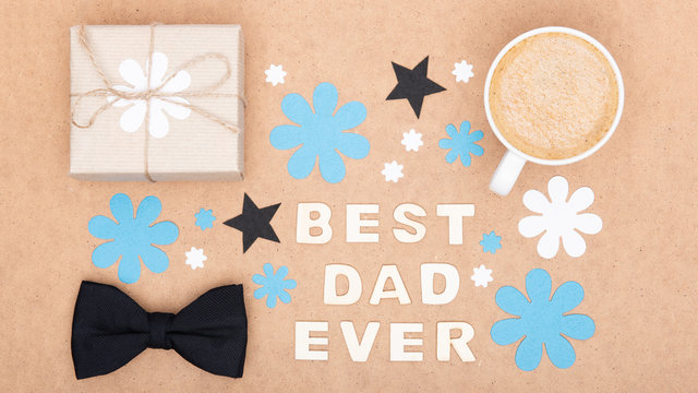 Happy Father's Day Background. Cup of coffee, beautiful present and black bow tie on brown background flat lay. Fathers day still life setup.