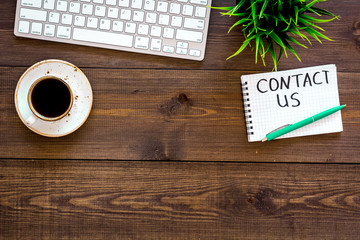 Template for contacts, background for contact information. Lettering Contact us in notebook on office work desk with computer on dark wooden background top view space for text