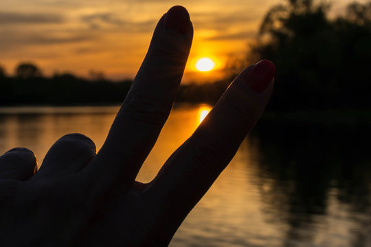 Woman's hand making peace sign at sunset