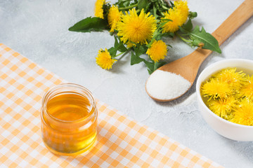 Ingredients for jam from dandelions. Fresh flowers of dandelions, sugar and water on a light summer background.