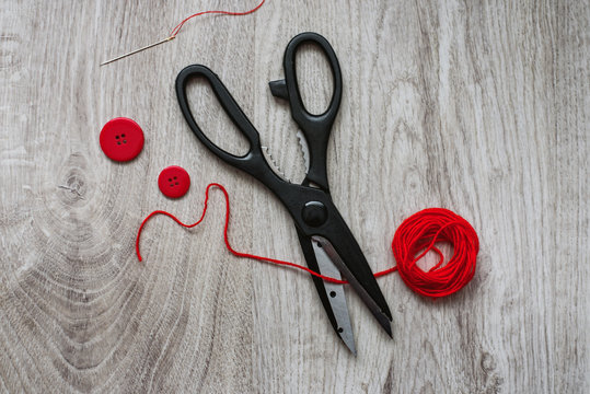Black steel scissors, red yarn ball and buttons for handmade work on a wooden background