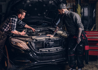 Fototapeta na wymiar Two mechanics check the car engine during repair in a garage.