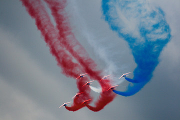 Several military aircraft symmetrically perform aerobatics figures releasing a multicolored smoke