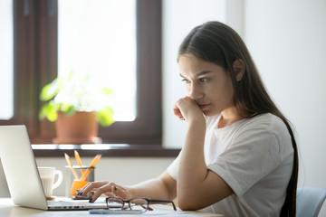 Concerned female worker looking at laptop screen suspiciously, thinking about problem solution,...
