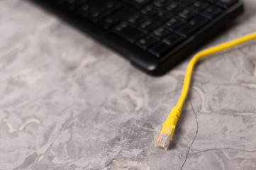 Yellow network cable for computer with plastic connector and black keyboard on old worn and scratched concrete floor with copy space