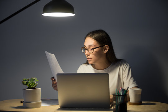 Female Student Getting Ready For Exam, Reading Paper Handout Material, Working At Laptop, Or Preparing Presentation At Night Under Lamp Light. Woman Taking Online Business Course In Small Home Office