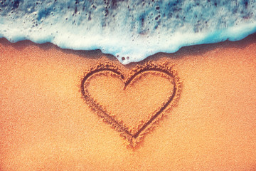 Heart on a sand of beach with wave on background