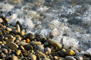 pebble stones on the sea beach, the rolling waves of the sea with foam