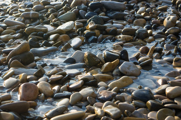 pebble stones on the sea beach, the rolling waves of the sea with foam