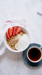 Perfect breakfast: crunchy granola with yoghurt and strawberries with a cup of black coffee on marble table