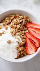 Perfect breakfast: crunchy granola with yoghurt and strawberries with a cup of black coffee on marble table