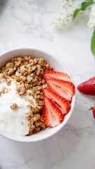 Perfect breakfast: crunchy granola with yoghurt and strawberries with a cup of black coffee on marble table