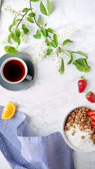 Perfect breakfast: crunchy granola with yoghurt and strawberries with a cup of black coffee on marble table. Flat lay with copy space