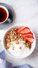 Perfect breakfast: crunchy granola with yoghurt and strawberries with a cup of black coffee on marble table