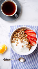 Perfect breakfast: crunchy granola with yoghurt and strawberries with a cup of black coffee on marble table