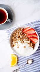 Perfect breakfast: crunchy granola with yoghurt and strawberries with a cup of black coffee on marble table