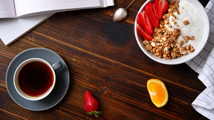 Perfect breakfast: crunchy granola with yoghurt and strawberries with a cup of black coffee on wooden table. Flat lay with copy space