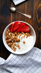 Perfect breakfast: crunchy granola with yoghurt and strawberries with a cup of black coffee on wooden table. Close up top view.