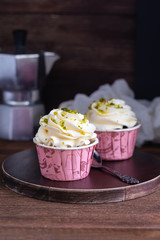 Homemade chocolate muffins or cupcakes with vanilla cream and pistachio on the wooden background