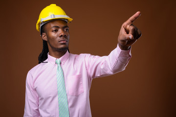 Young handsome African businessman with hardhat against brown ba